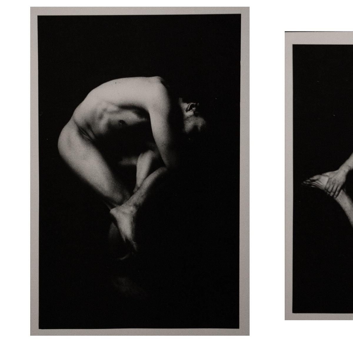 A nude man is curled up on a dark background with his head tilted back.