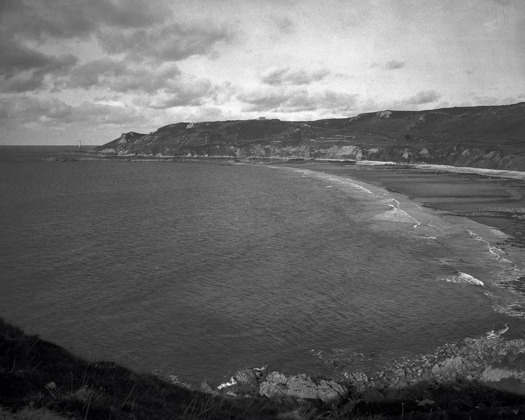 A wide bay with a sandy beach and cliffs is visible under a cloudy sky.
