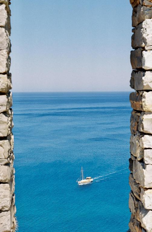 A sailboat moves across a vast blue ocean, framed by two stone walls.