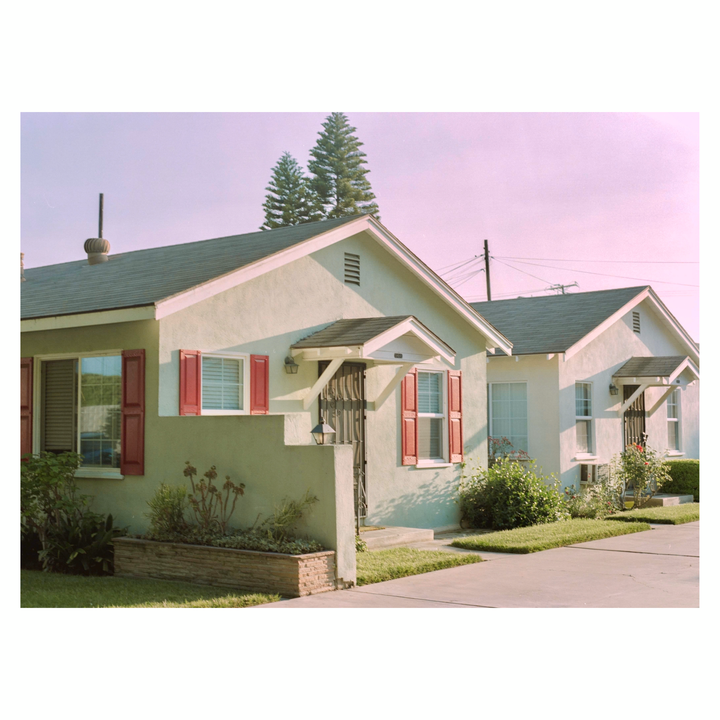 Two small houses with red shutters and green roofs are visible under a pink sky.