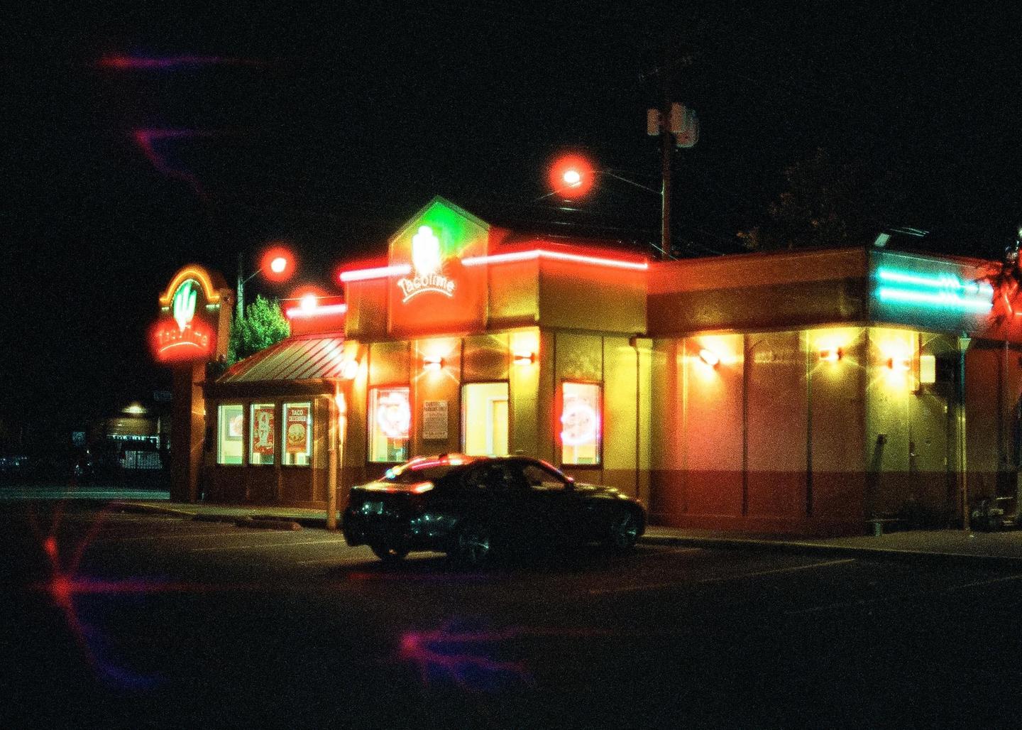 A car is parked in front of a Taco Time restaurant at night.