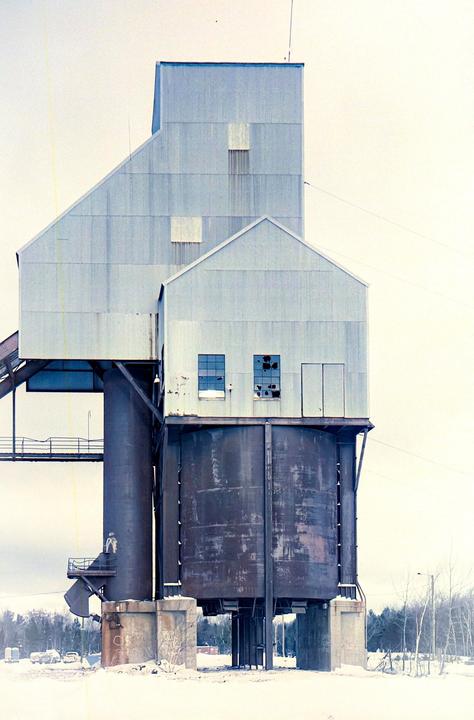 A large industrial structure with silos and corrugated metal buildings stands in a snowy landscape.