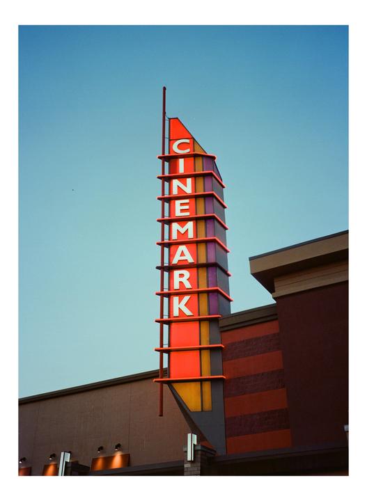A tall, colorful Cinemark sign stands against a clear blue sky next to a building.