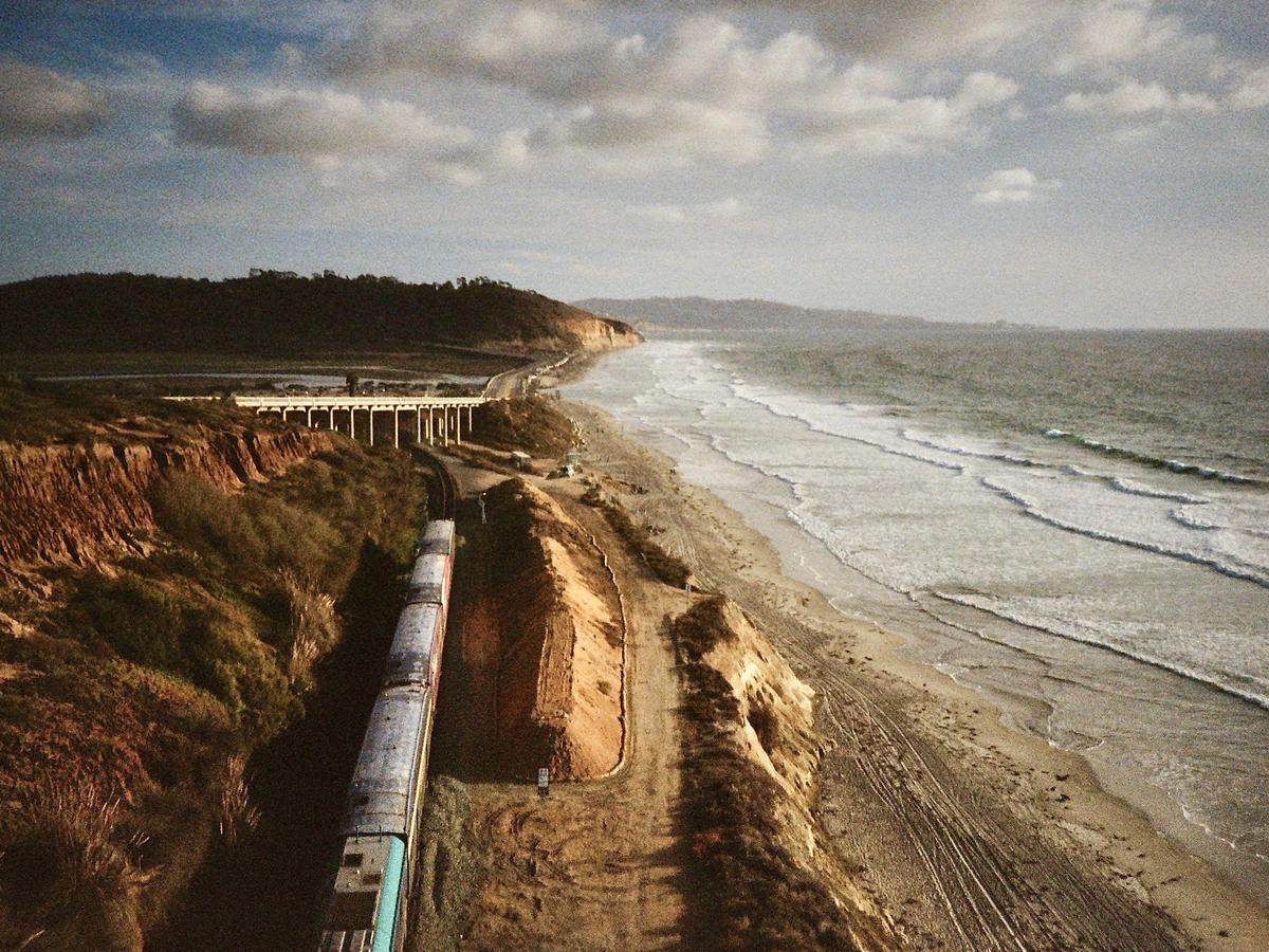 A train travels along a track next to a beach with waves crashing on the shore.