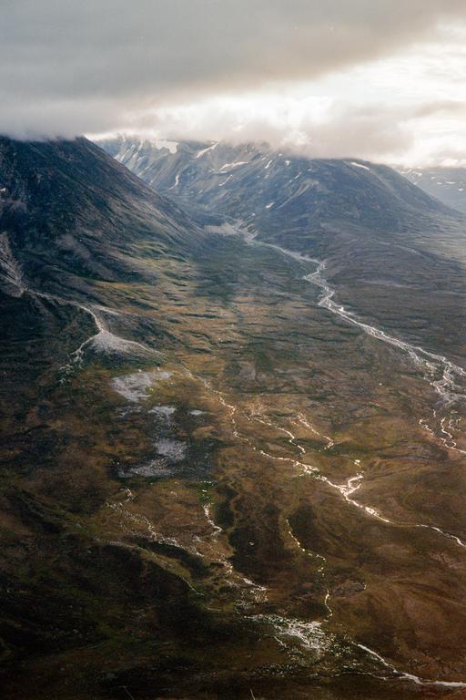A winding river flows through a valley surrounded by mountains with clouds obscuring their peaks.