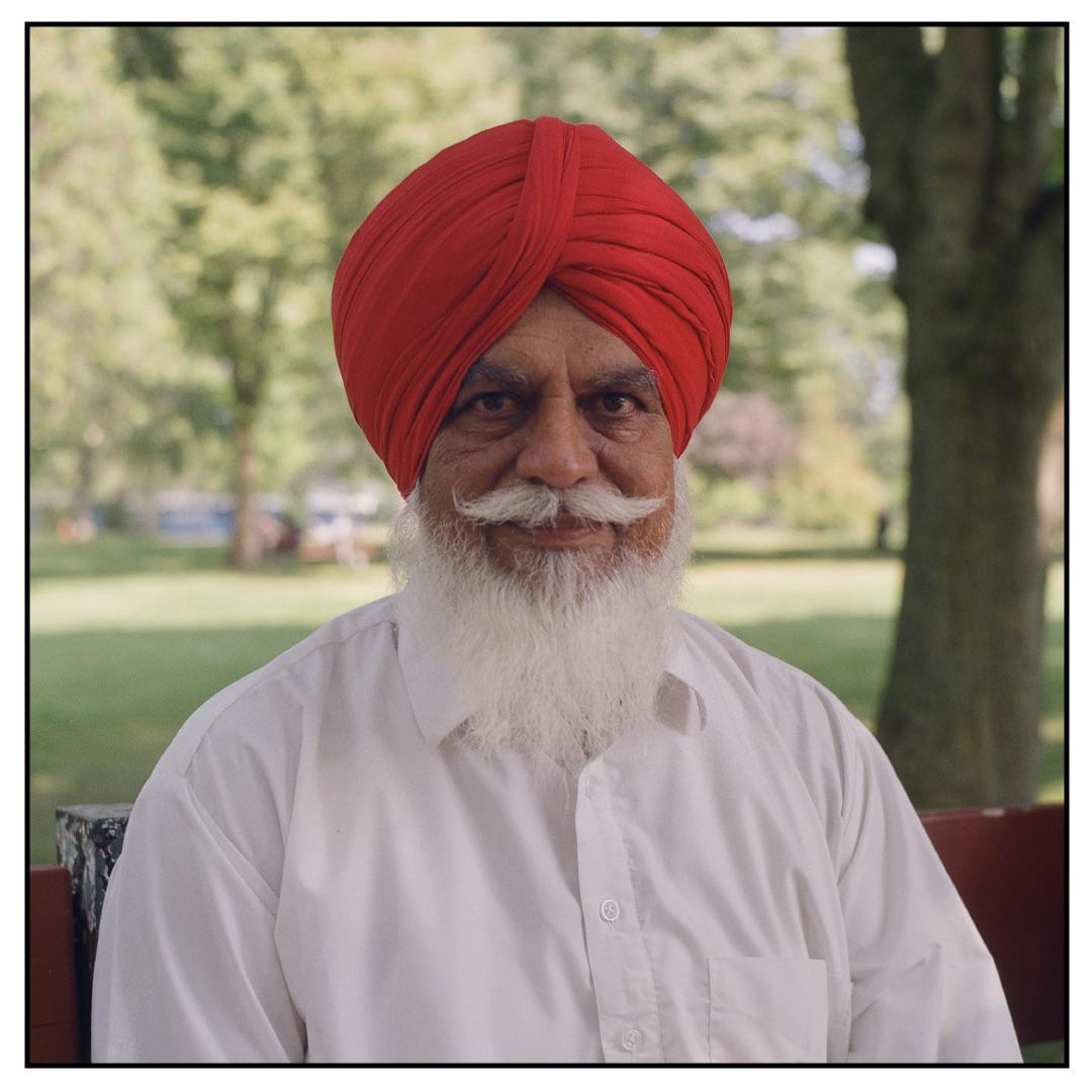 A man with a red turban and white beard sits outdoors.