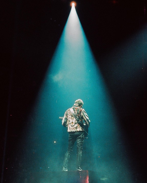 A musician stands on a stage, illuminated by a single spotlight from above.