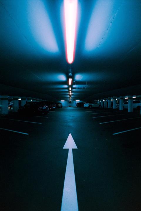 A white arrow on the ground points towards the end of a parking garage illuminated by blue and red lights.