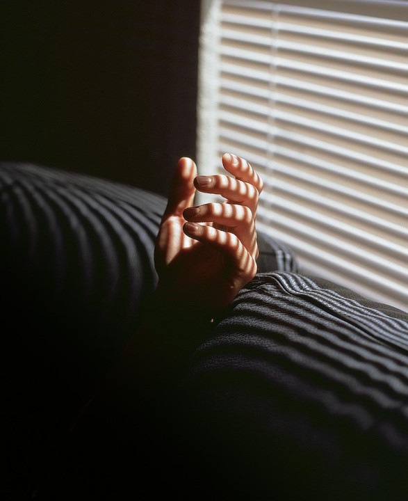 A hand is illuminated by sunlight streaming through window blinds, casting striped shadows on the hand and a dark surface.