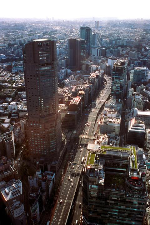 An aerial view shows a highway winding through a dense urban landscape with numerous buildings and a hazy sky.