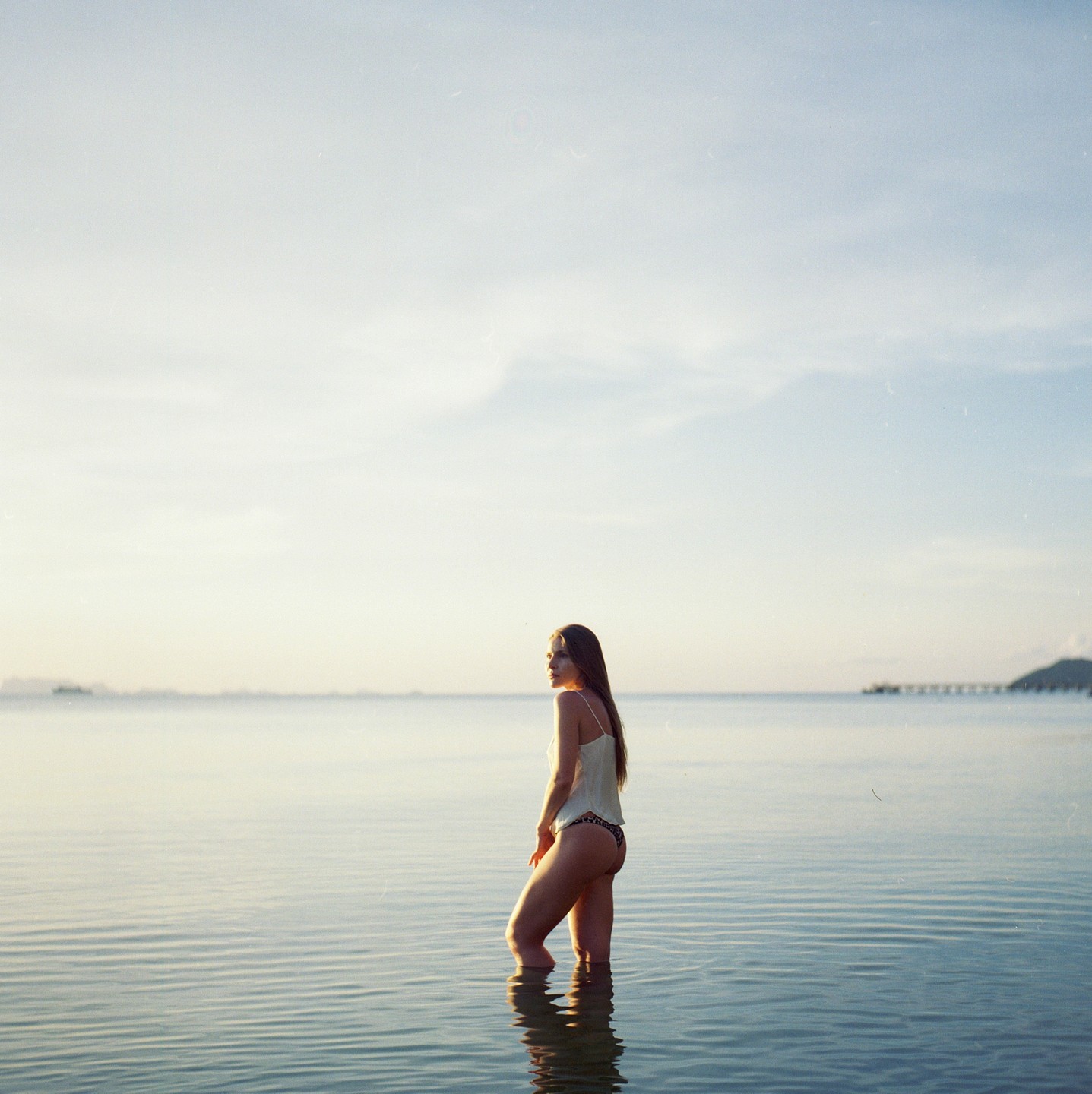 A woman stands in the ocean looking towards the horizon at dusk.
