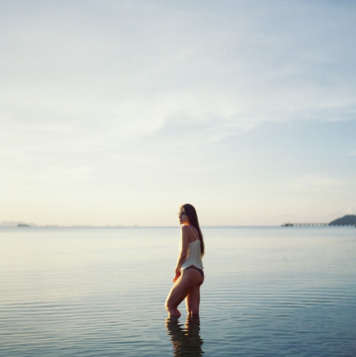 A woman stands in the ocean looking towards the horizon at dusk.