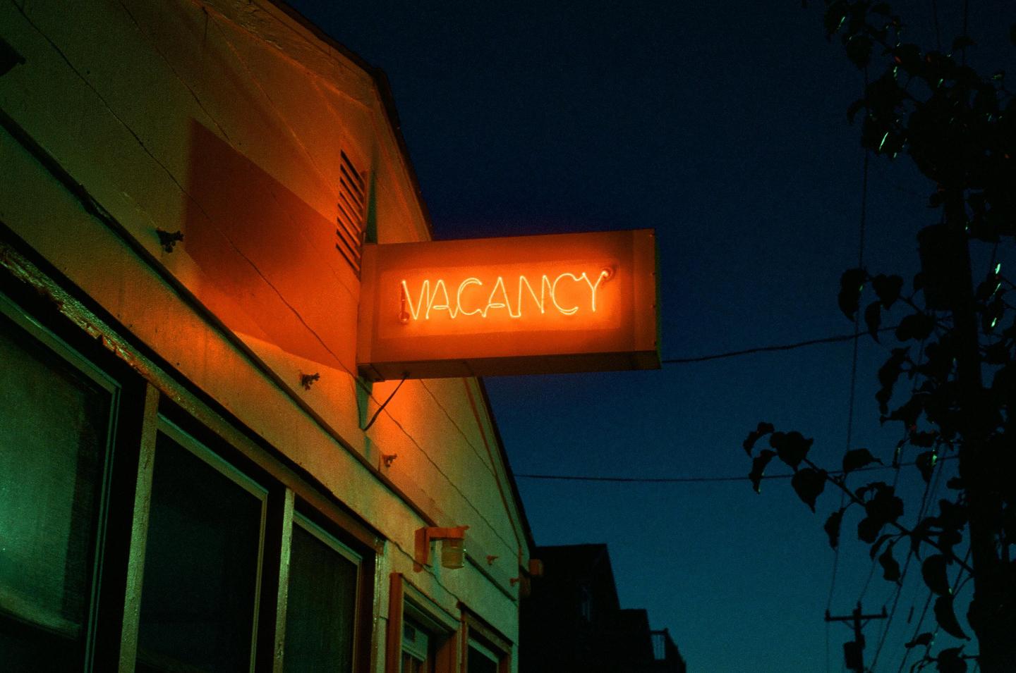 A neon "VACANCY" sign glows orange on the side of a building at night.