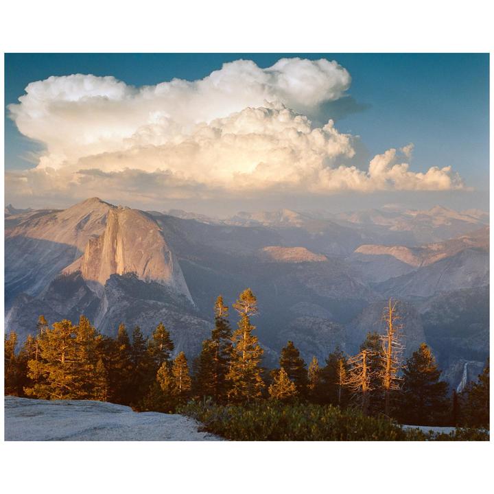 A large rock formation rises above a forest with clouds in the sky.