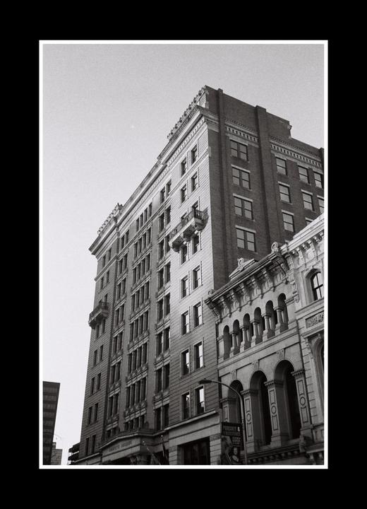 A tall building with many windows and ornate architectural details stands next to another building with arched windows.