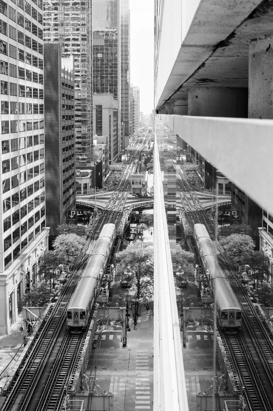 A train travels on elevated tracks through a city with tall buildings and a reflection of the scene on a nearby building.