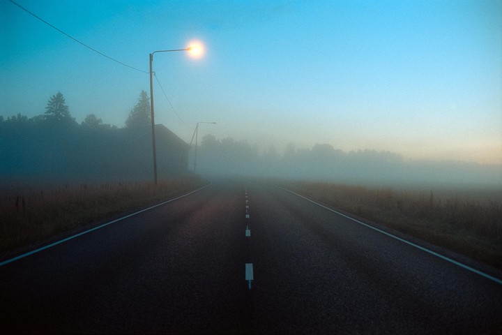 A road stretches into the distance, illuminated by a single street light in a hazy, blue-tinged landscape.