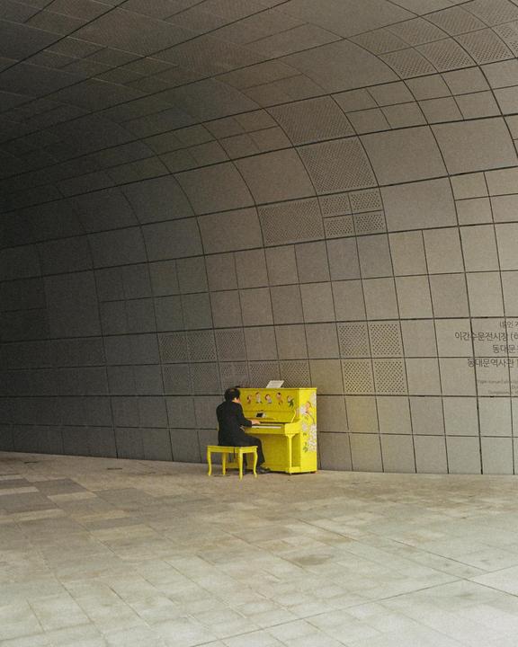 A man plays a bright yellow piano with floral designs in a modern, curved building.