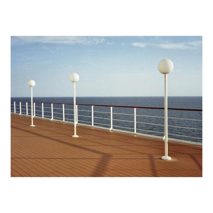 Three white lampposts stand on the deck of a cruise ship, overlooking the ocean under a clear sky.