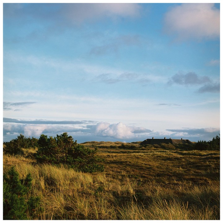 A house with chimneys is nestled into a grassy hill under a blue sky with clouds.