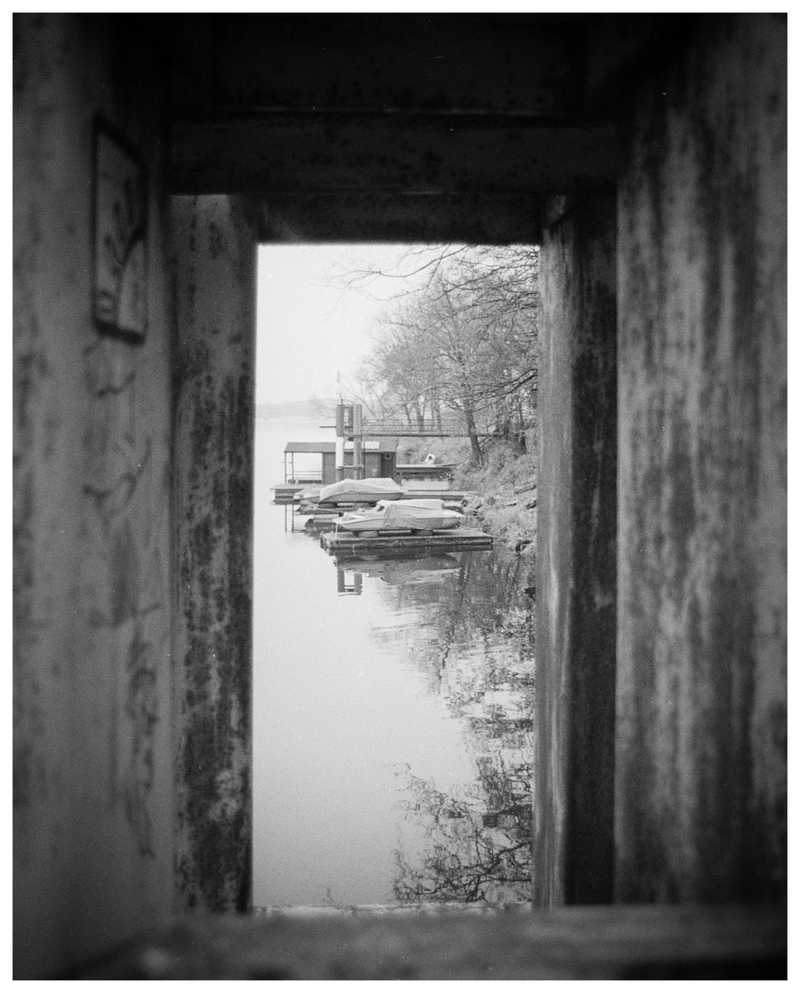 A river with boats docked along the bank is framed by a concrete structure.