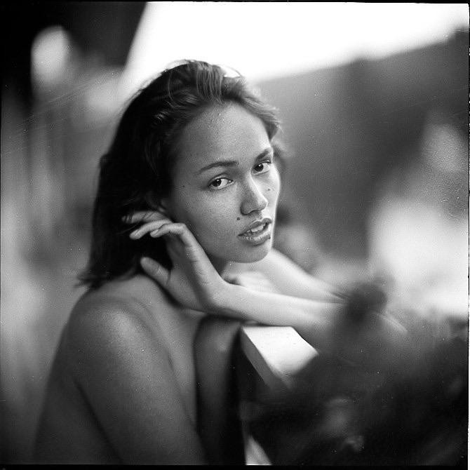 A woman with dark hair looks over her shoulder, resting her arm on a railing.