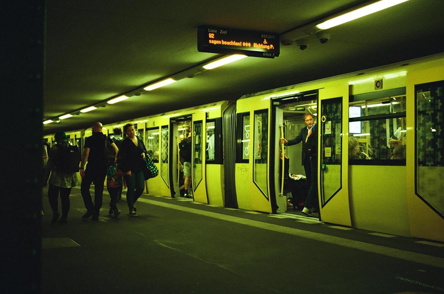People walk along a subway platform as a man stands in the open door of a subway car.