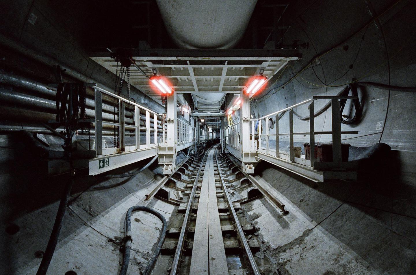 A long tunnel with train tracks in the center is illuminated by red lights.