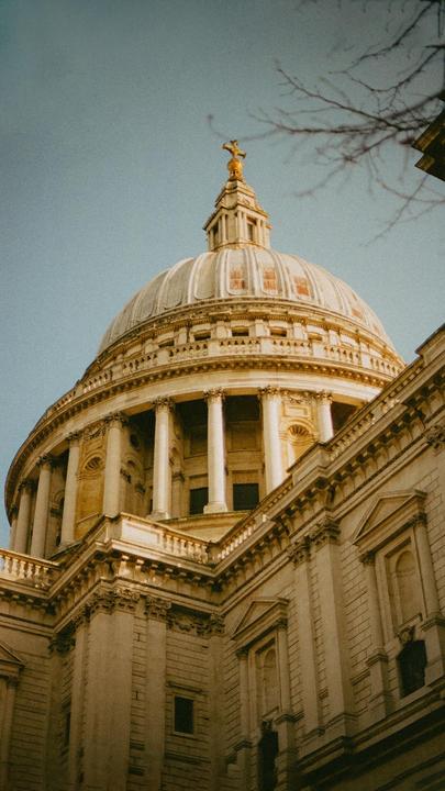 A large domed building with columns and intricate architectural details is viewed from below against a clear sky.