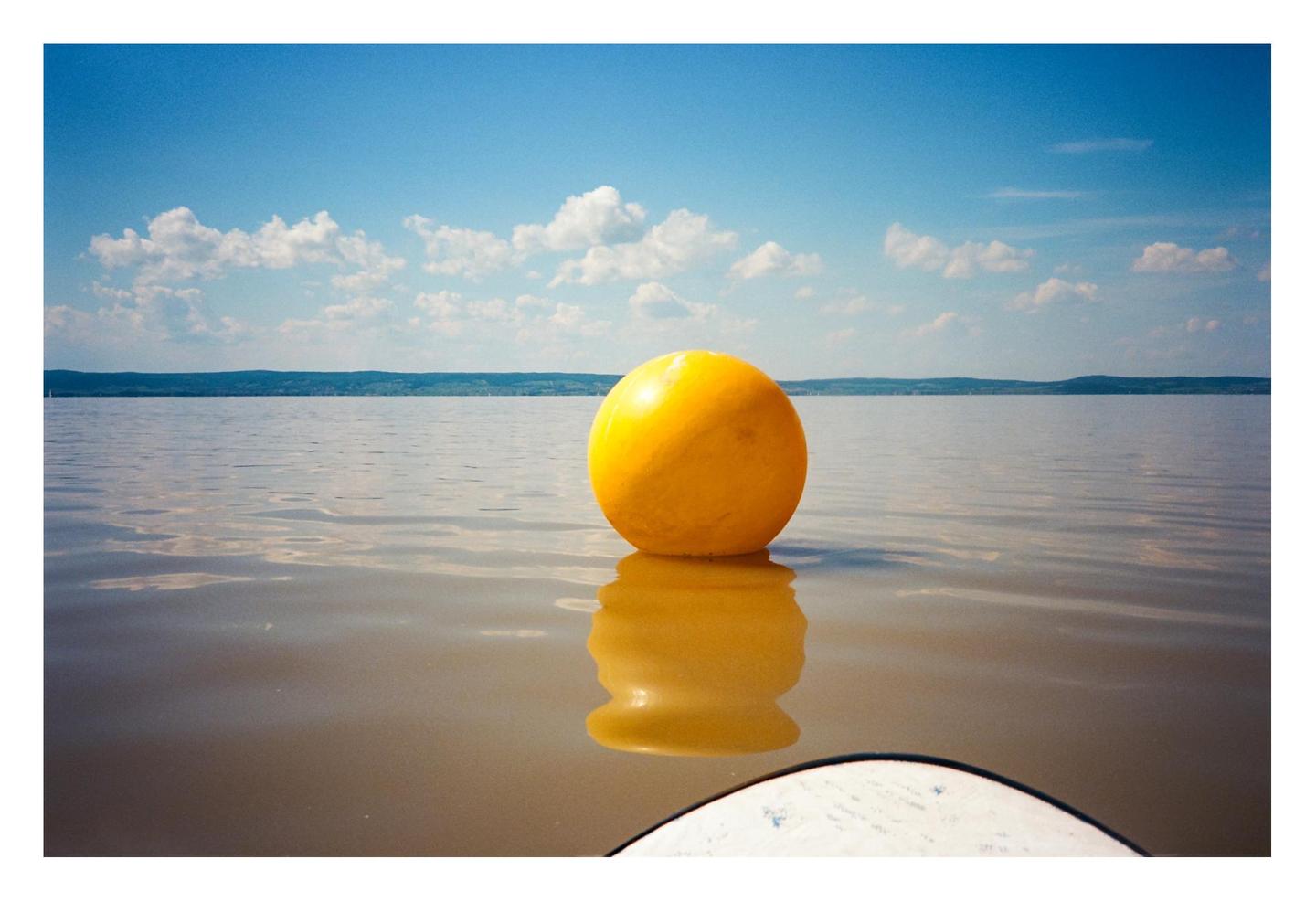 A yellow buoy floats on the water under a blue sky with white clouds.