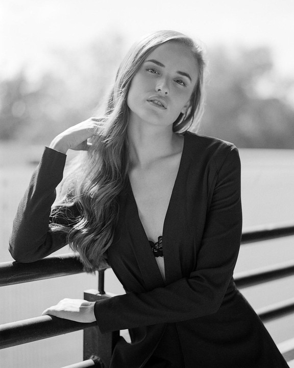 A woman with long hair and a dark jacket leans on a railing.