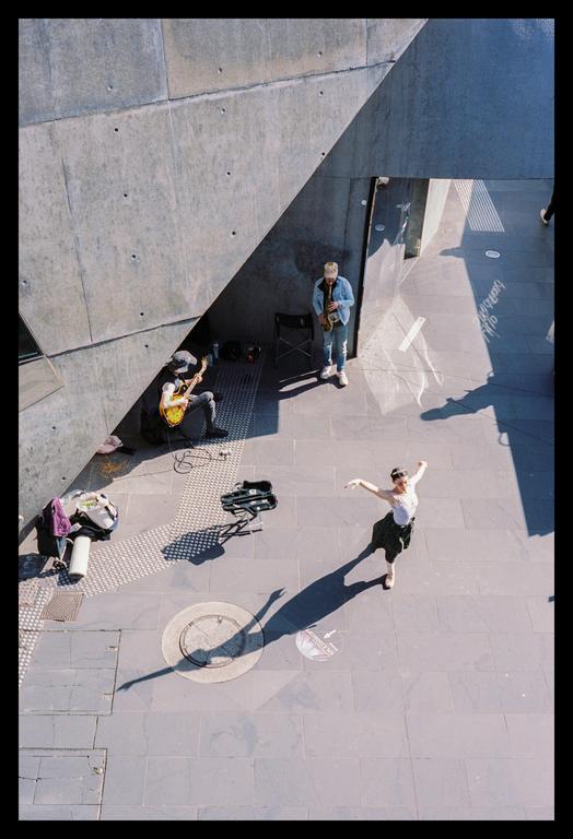 Three people are busking on a concrete street with strong shadows.
