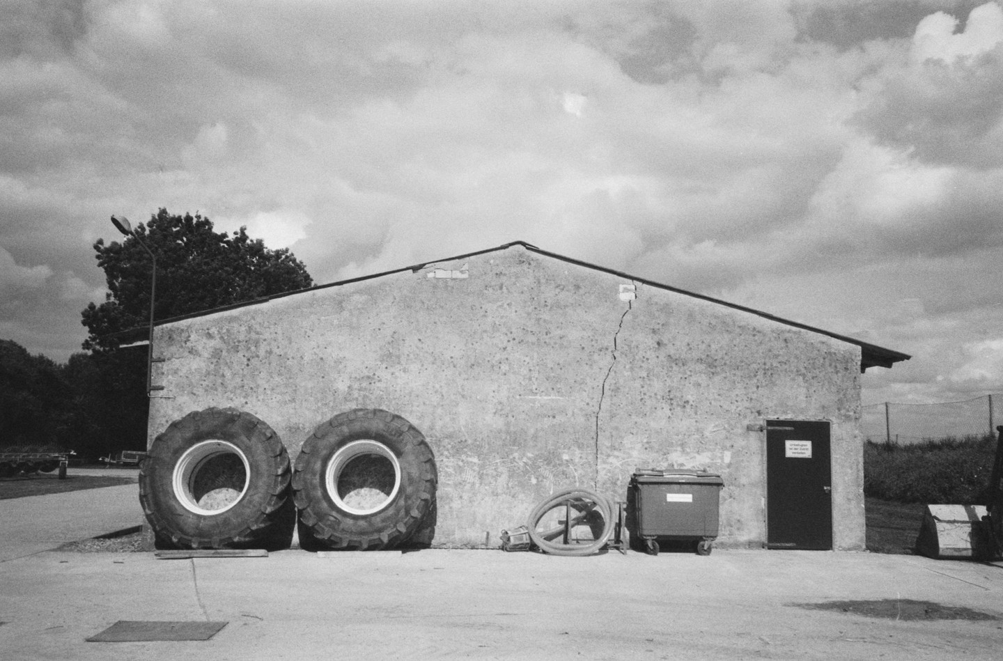Two large tires lean against a barn with a cracked wall under a cloudy sky.