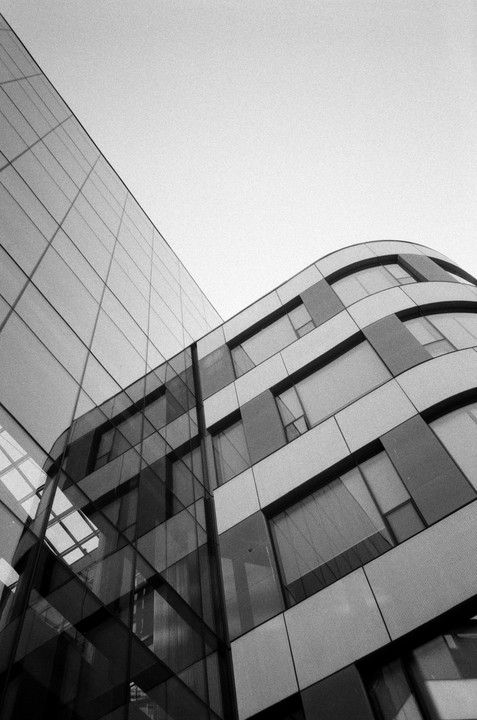 A low-angle view shows the curved facade of a modern building with a glass exterior and a clear sky.