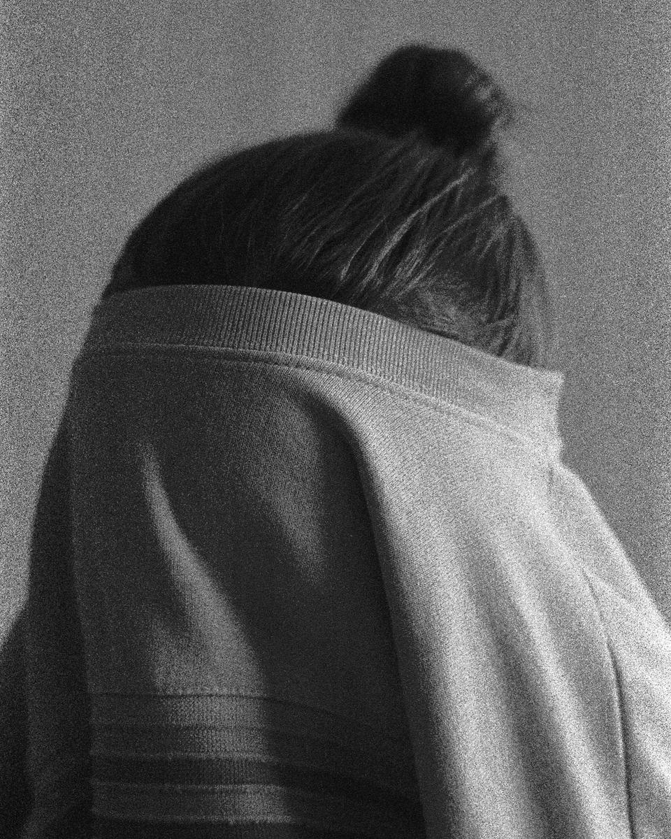 A person with a bun in their hair is seen from behind, wearing a sweater pulled up to cover their head.
