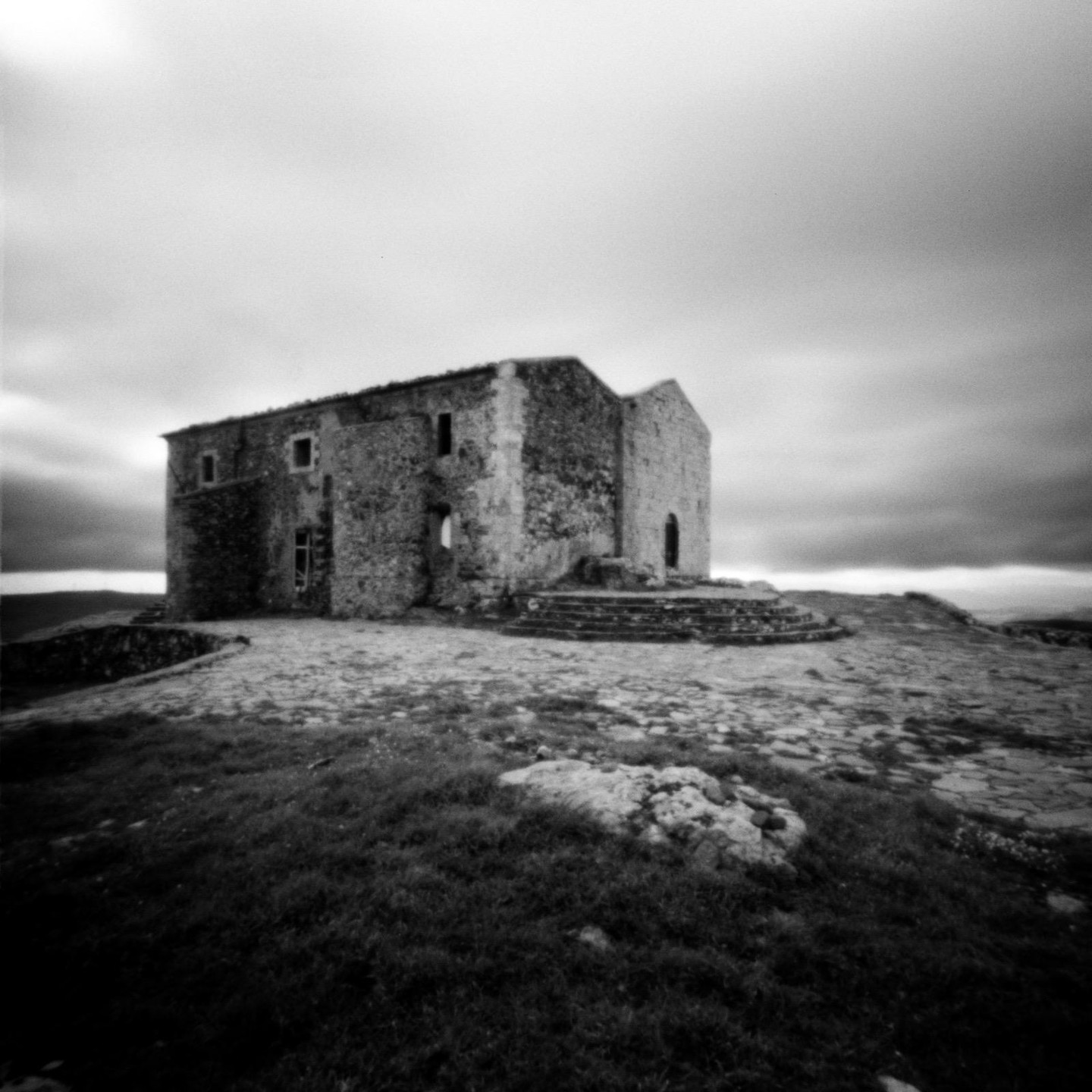 An abandoned stone church stands on a hill under a cloudy sky.