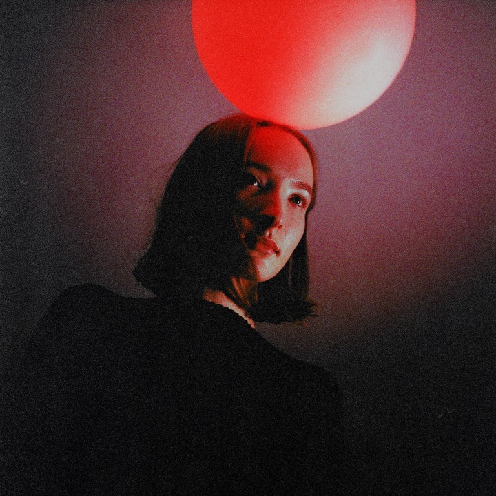A woman with short hair looks up at a red light source above her head.