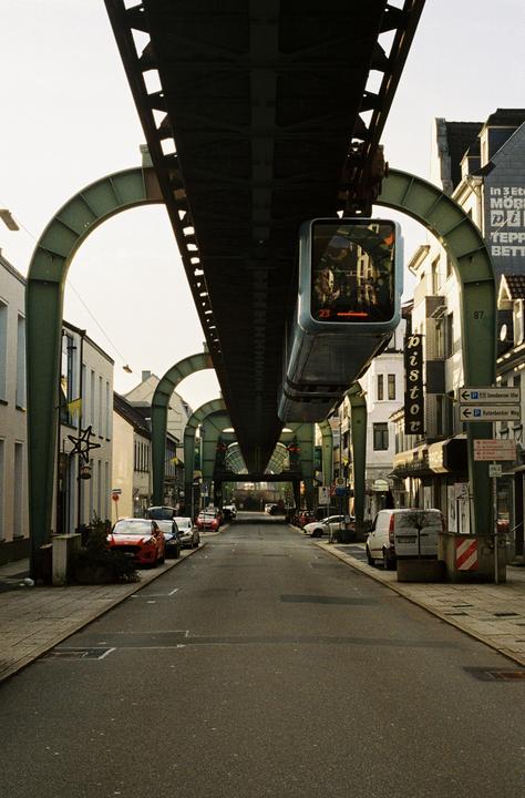 A street in Wuppertal, Germany, is pictured with a suspended monorail train passing overhead.