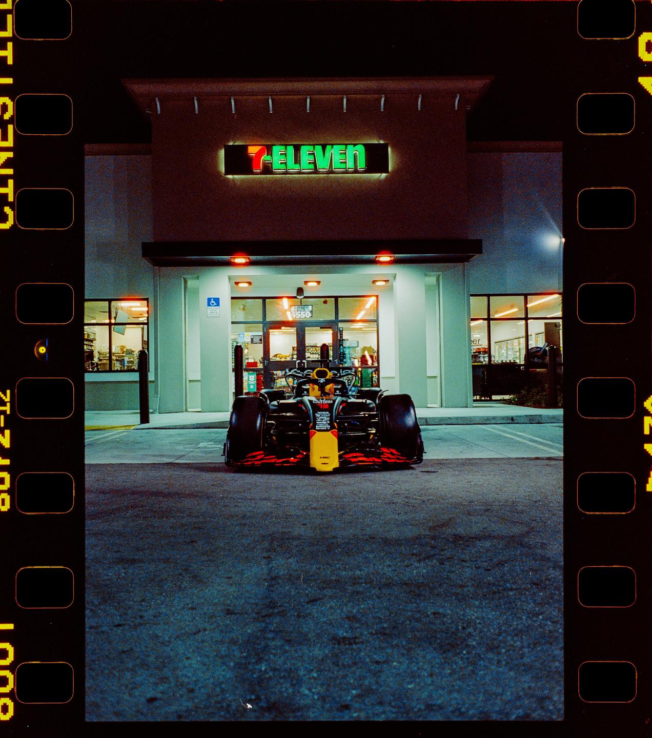 A formula one race car is parked in front of a 7-Eleven convenience store at night.