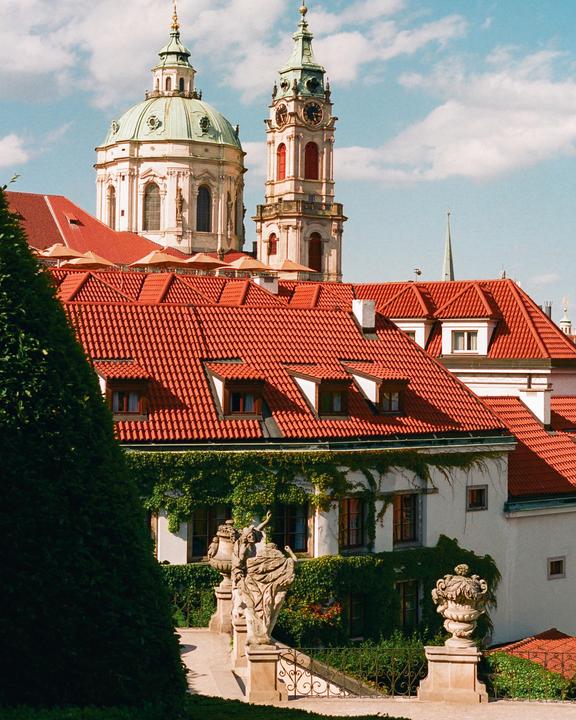 A view of red-tiled rooftops and a building covered in ivy, with a domed church and clock tower in the background.