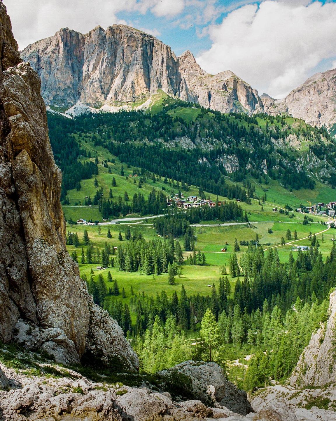A valley with a village and forest is nestled between two large mountains.
