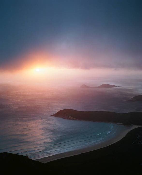 The sun sets over a bay with islands in the distance.