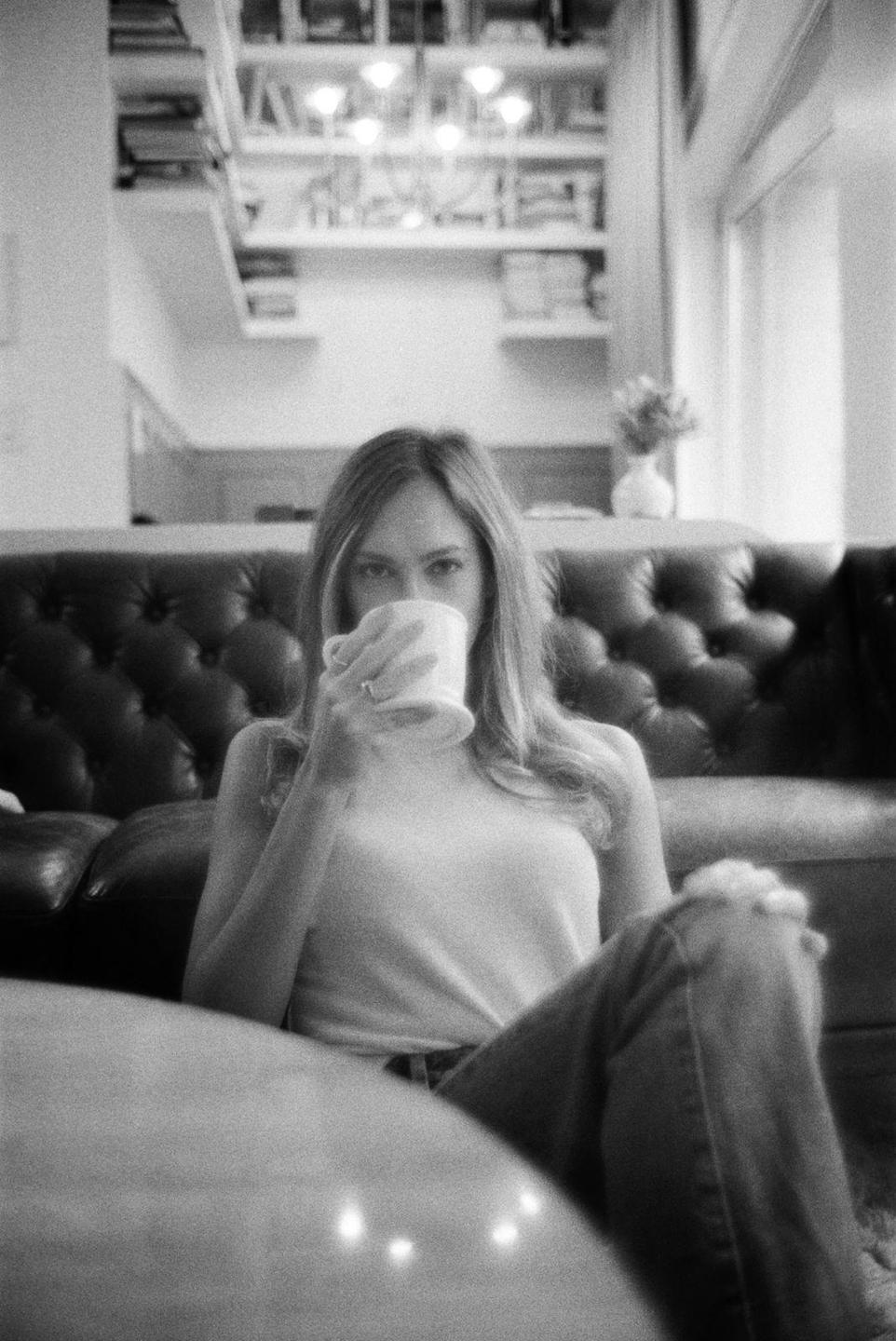 A woman sits on the floor in a living room, drinking from a mug.
