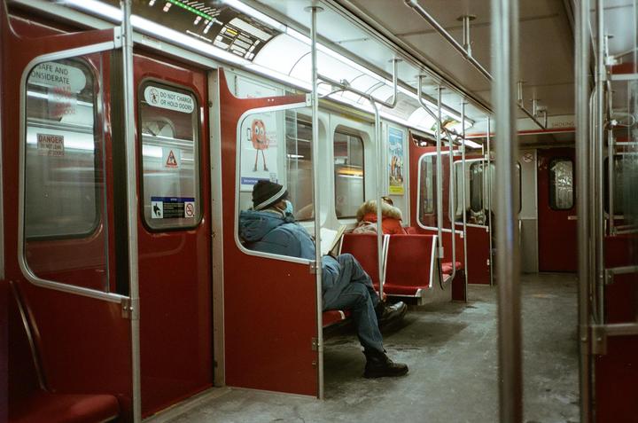 A man in a blue jacket and a woman in a red jacket sit on a subway train.