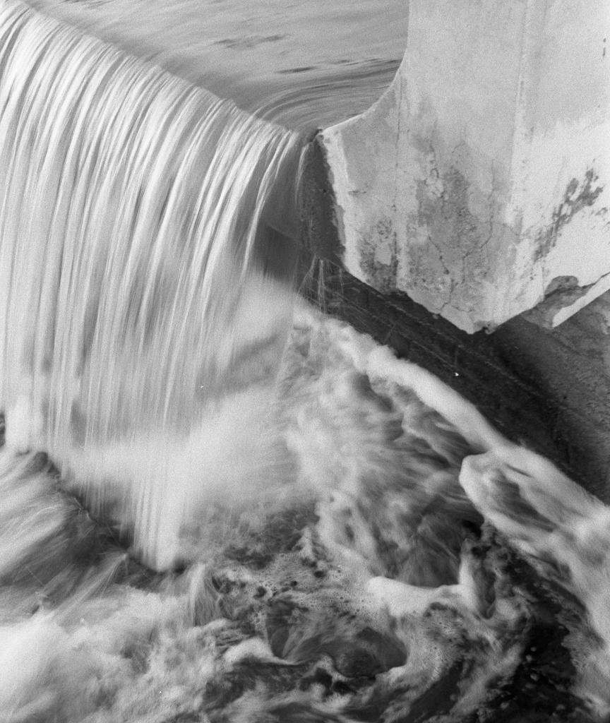 Water cascades over a concrete structure, creating foam and turbulence below.