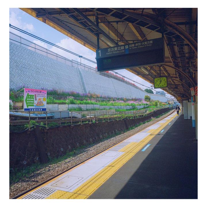 A train station platform with a person walking in the distance and a wall covered in flowers.