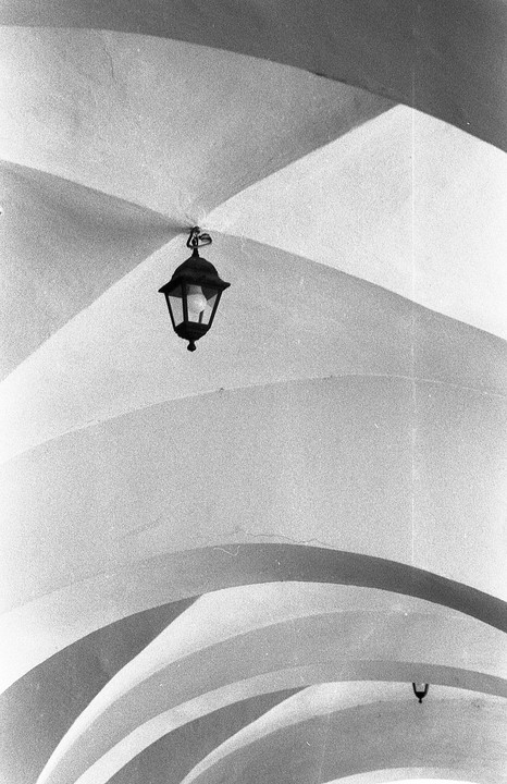 A black lantern hangs from a white arched ceiling with strong shadows.