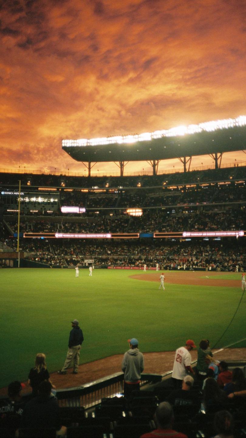 A baseball game is being played in a stadium under a dramatic orange and red sky.