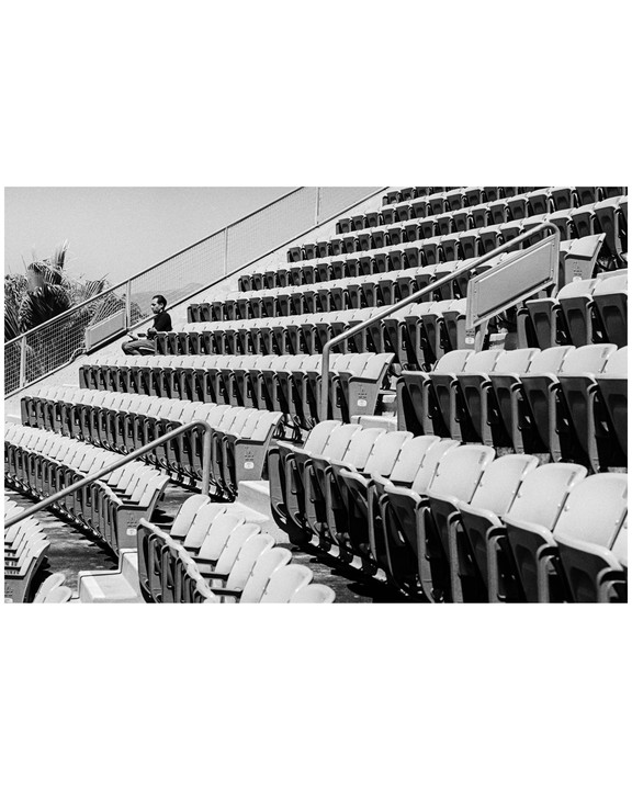 A man sits alone in the upper rows of an empty stadium.