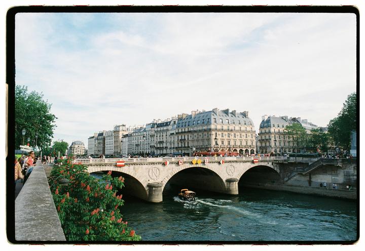 A boat travels on the river Seine with a bridge and buildings visible in the background.